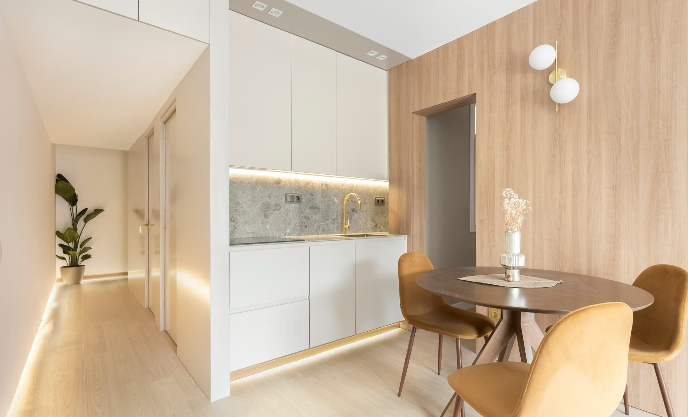 Interior de una reforma de Urbanovo: paso de la cocina al comedor con paneles de madera y detalles en latón